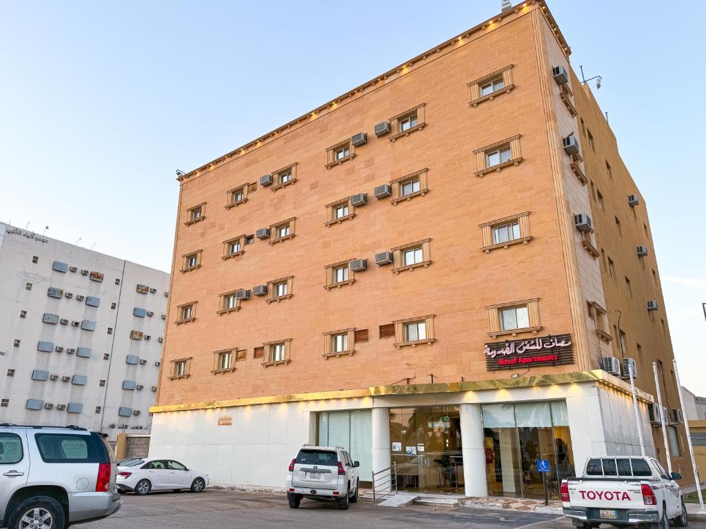 a large brick building with cars parked in a parking lot at Masaf apartment in Al Mithnab