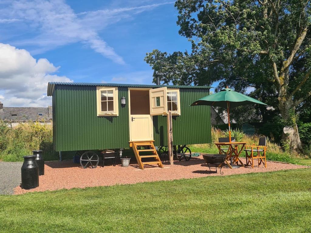 a green tiny house with a table and an umbrella at Shepherd's Hut in heart of the Brecon Beacons in Bwlch