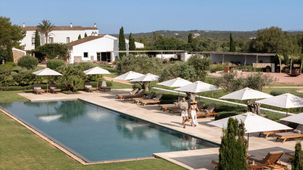 a pool at a resort with umbrellas and people standing near it at Torralbenc, a Small Luxury Hotel of the World in Cala en Porter