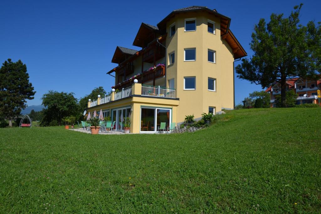 a large yellow building on a hill with a green field at Pension Haus Claudia in Drobollach am Faakersee