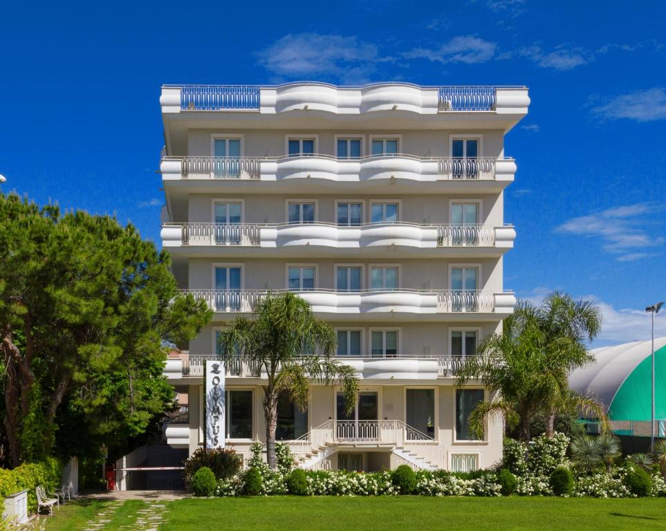 ein hohes weißes Gebäude mit Bäumen davor in der Unterkunft Olympus Resort in Alba Adriatica