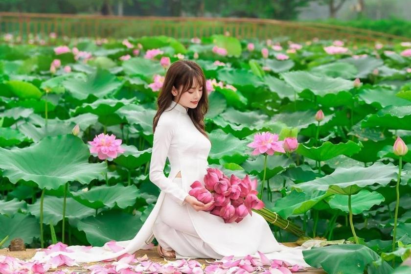 a woman in a white dress holding a bunch of flowers at Đầm sen Resort in Hòa Lạc