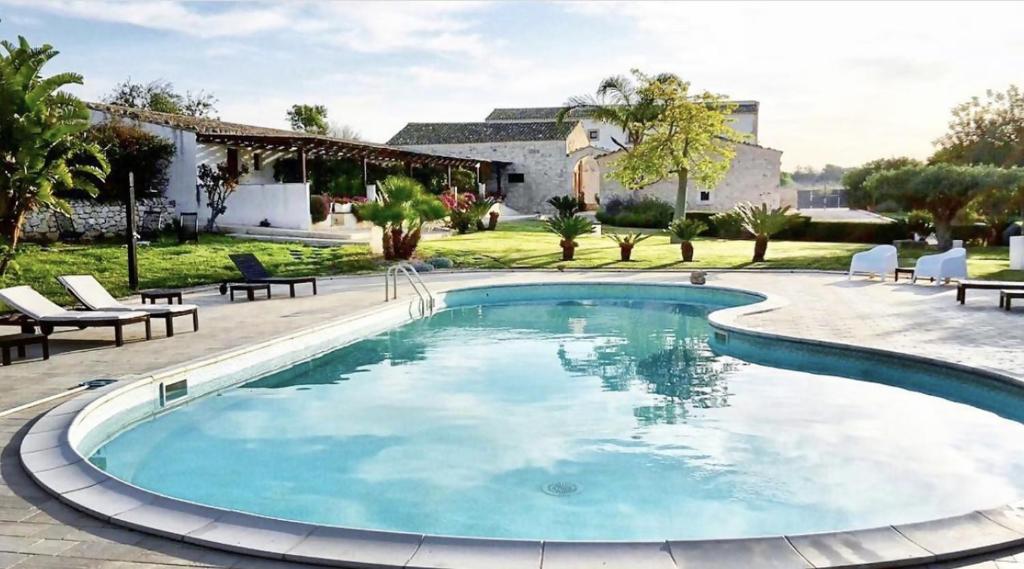 een zwembad in een tuin met stoelen en een huis bij Torre Dantona Country Suites in Pozzallo