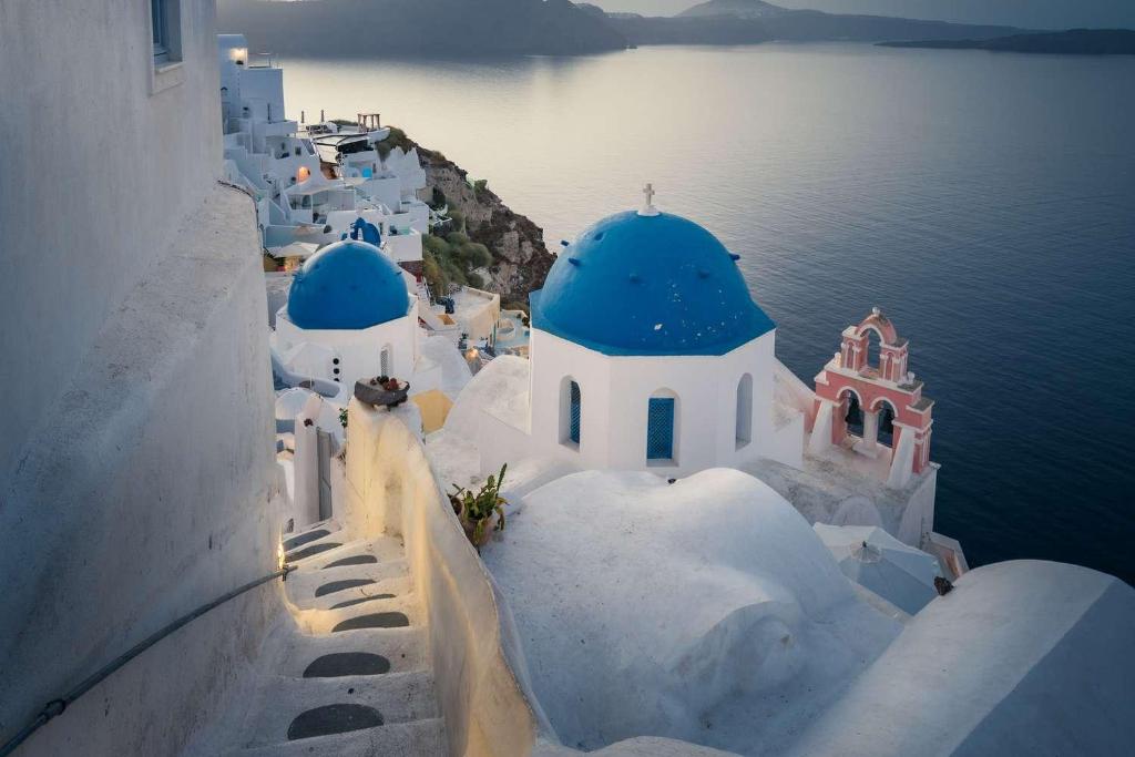 a group of white buildings with blue domes on the water at Oia Luxury villaes vacations in Oia
