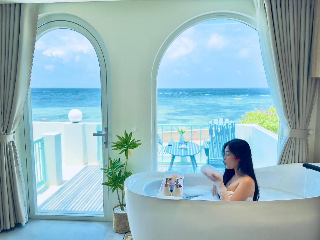 a woman sitting in a bath tub with a view of the ocean at Villa Đại Dương View Biển Đảo Phú Quý in Cu Lao Thu