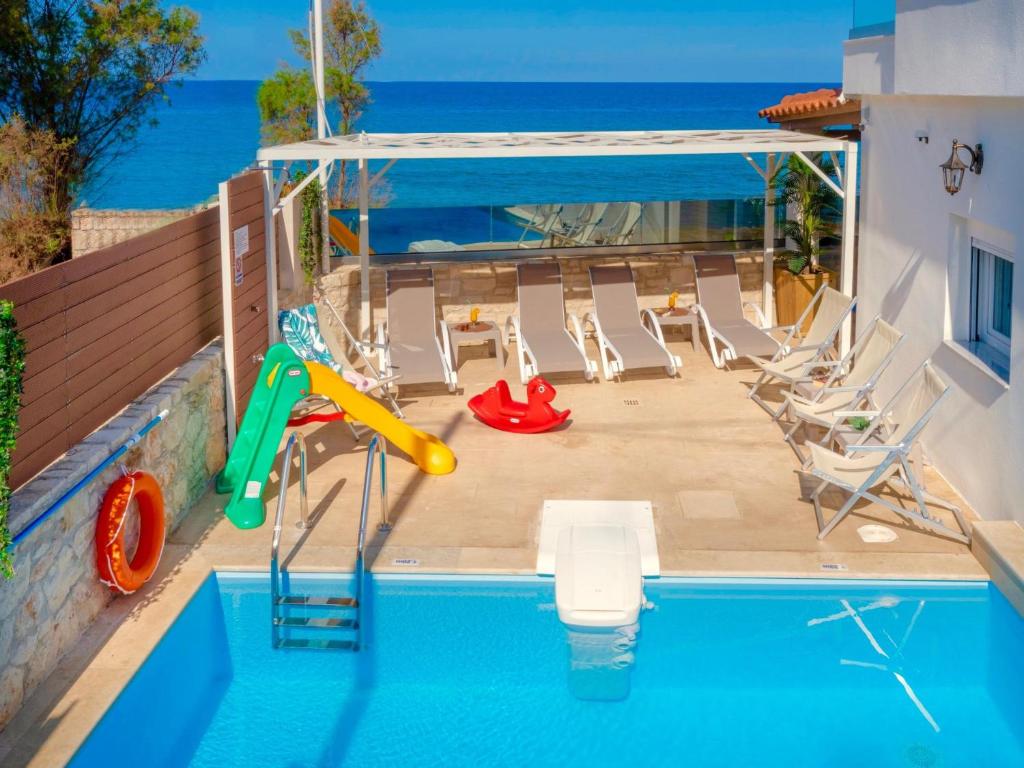 a pool with a slide and chairs and the ocean at Thalassa Beachfront Villa with private pool in Skaleta