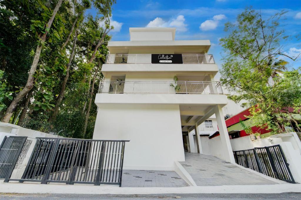 a white building with a balcony and trees at Super Collection O Valiyavila Junction Formerly Prism Heights in Trivandrum