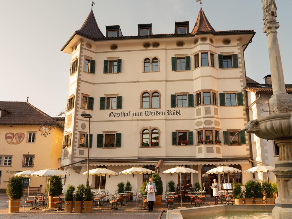 a large building with tables and umbrellas in front of it at Weisses Rössl in Caldaro