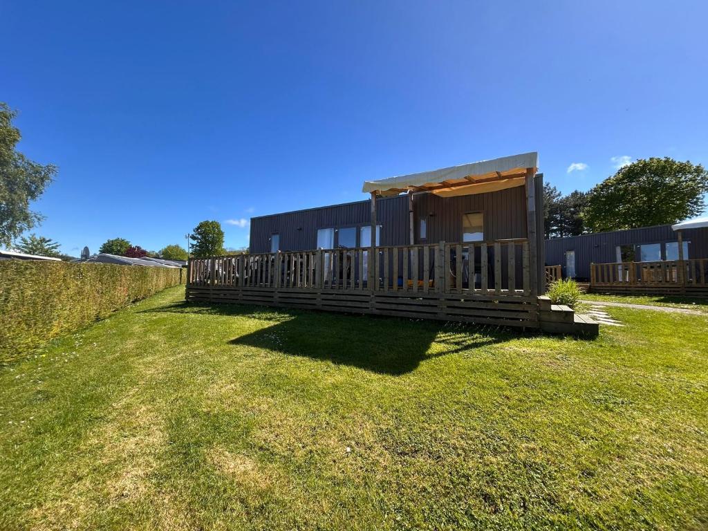 a house with a wooden deck in the grass at Houlgate - 254 - RARE VUE MER Magnifique Mobilhome 6 pers 3 chambres 2 SDB sur Camping 5 étoiles in Houlgate