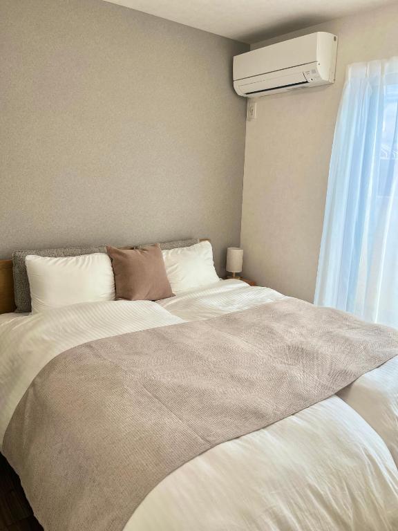 a bedroom with a large white bed with a air conditioner at VJ House in Fukuoka