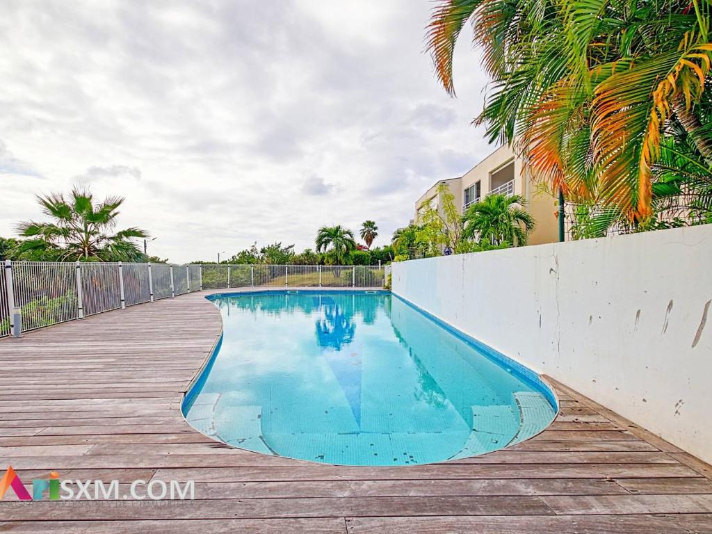 a swimming pool next to a fence and palm trees at Appartement cosy à Grand Case, proche plage, piscine, parking et Wi-Fi inclus - FR-1-734-77 in Marigot