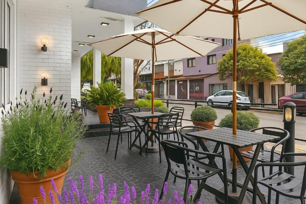 eine Außenterrasse mit Tischen, Stühlen und Sonnenschirmen in der Unterkunft Hotel San José in Villa Carlos Paz