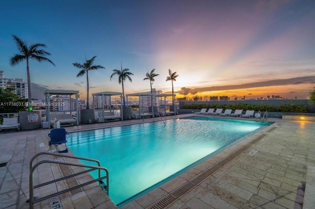 a large swimming pool with palm trees and a sunset at Hotel Miami Beach Convention Center in Miami Beach