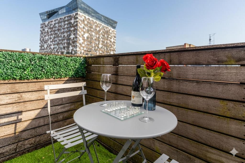 a table with two wine glasses and a vase with red roses at Central 2Bed,2Bath, Balcony Apartment Near New Street, Mailbox & Canals at Skyline Apartments in Birmingham