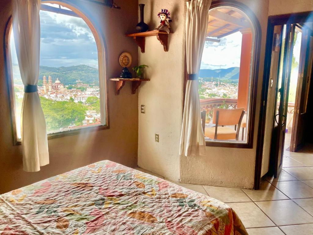 a bedroom with a bed and two windows with a view at Entre el sol y la luna in Taxco de Alarcón