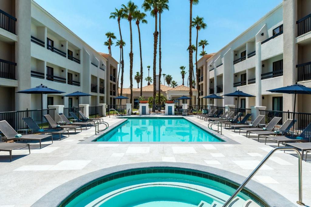 una piscina en un hotel con sillas y sombrillas en Courtyard by Marriott Palm Springs, en Palm Springs