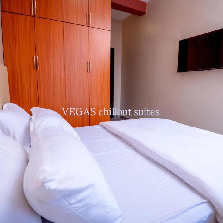 a bedroom with a bed with white pillows and a tv at Vegas Suites and SPA in Kampala
