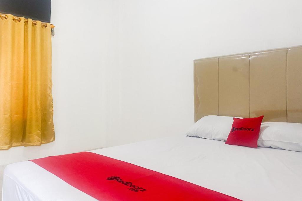 ein Schlafzimmer mit einem weißen Bett mit einem roten Kissen in der Unterkunft RedDoorz at Risma Hostel ITERA Lampung in Kedaton
