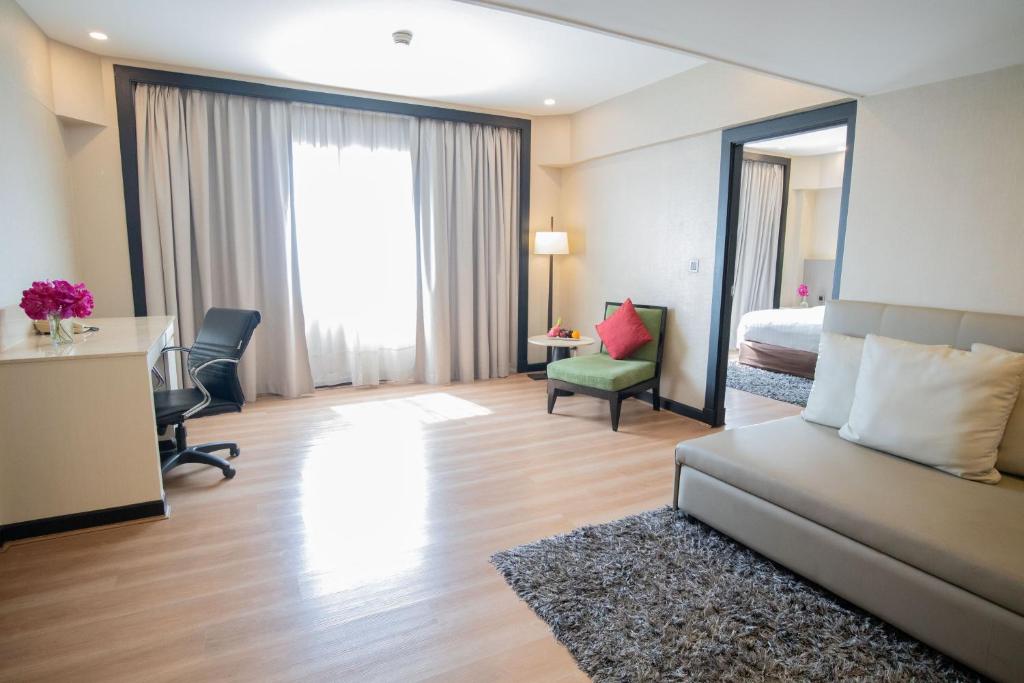 A spacious room with a dedicated desk, sofa, armchair and heavily curtained window.