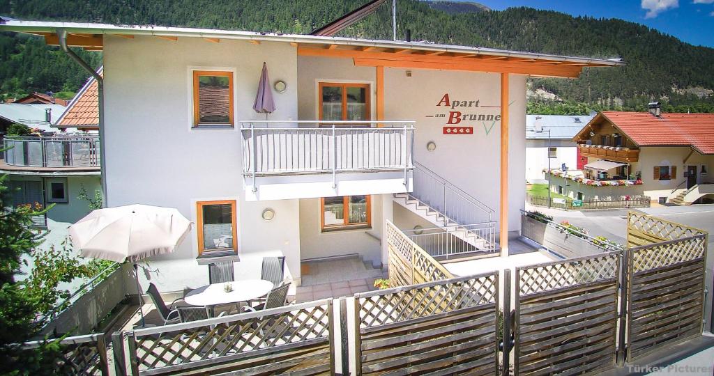 un edificio con balcón con mesa y sombrilla en Apart am Brunnen, en Ried im Oberinntal