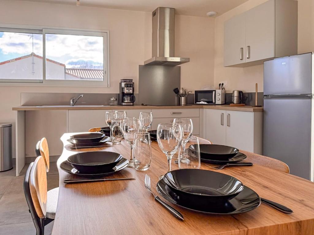 a kitchen with a wooden table with plates and wine glasses at Maison 2 ch-6 pers parking & jardin in La Pommeraie-sur-Sèvre