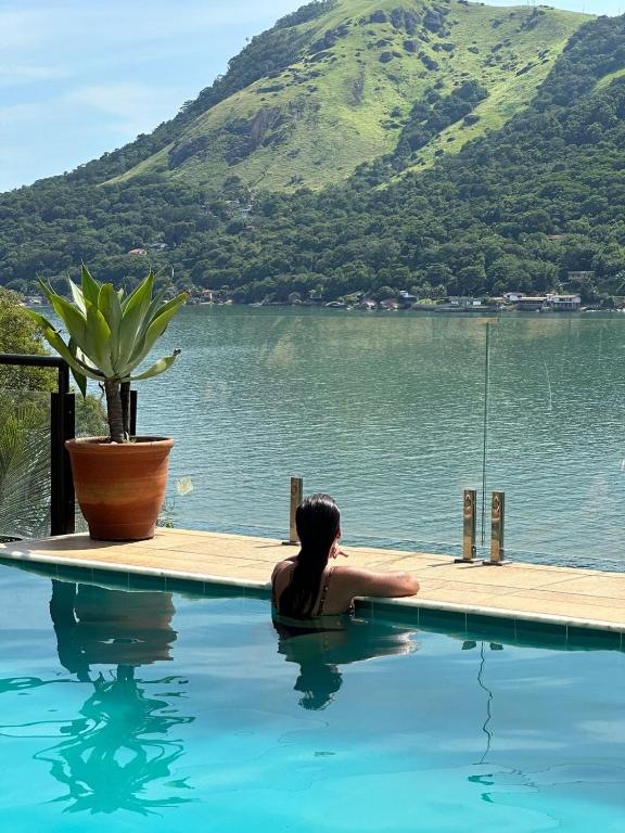a woman sitting in a swimming pool next to a lake at Pousada Costa dos Corais in Mangaratiba