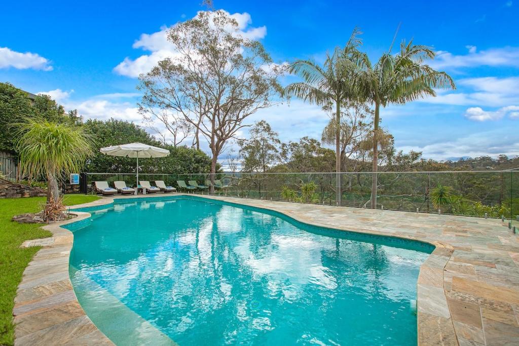 a swimming pool in a yard with chairs and an umbrella at Garigal Retreat with Pool access in Forestville