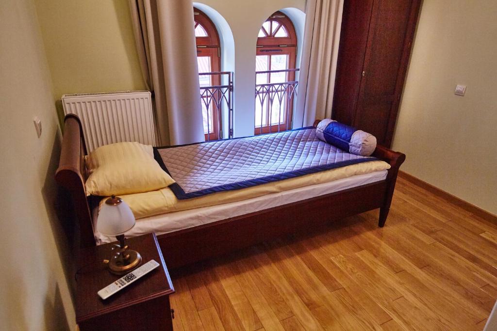 Cama pequeña en habitación con 2 ventanas en Centrum Obsługi Turysty Kordegarda, en Raczki