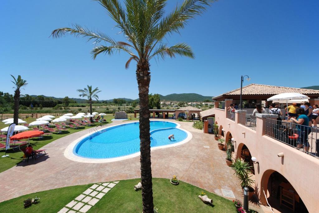 un complexe avec un palmier et une piscine dans l'établissement Alma Resort, à Castiadas