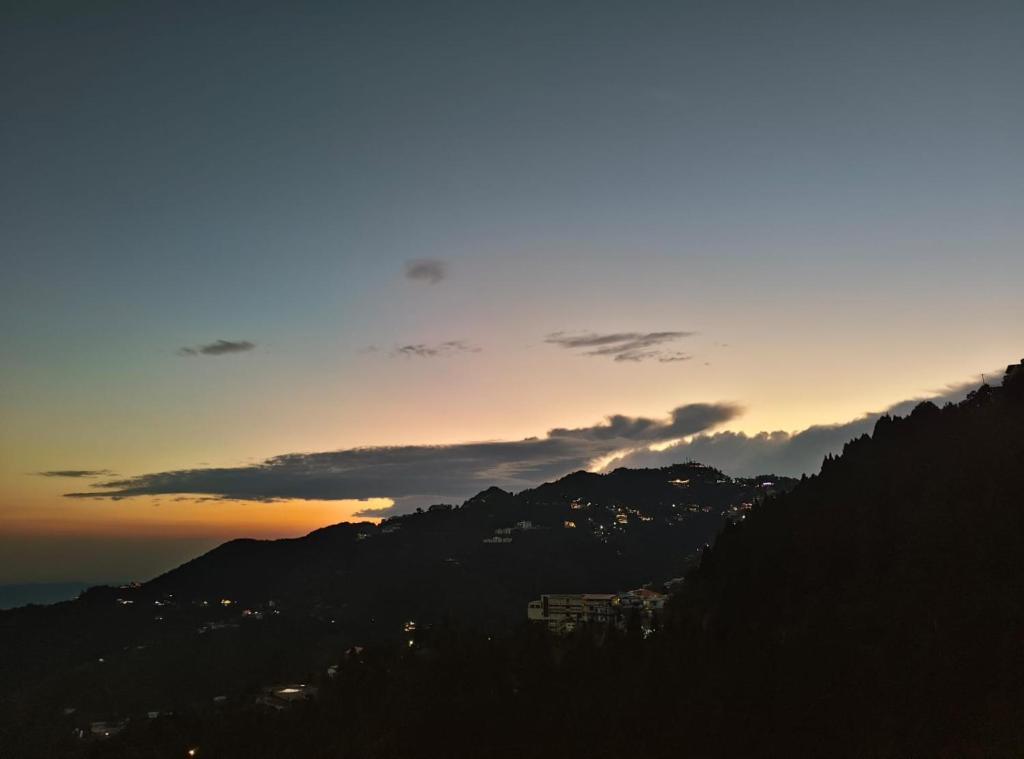 a sunset over a mountain range with a city at Aagman Homestay & Rooftop Restaurant in Mussoorie