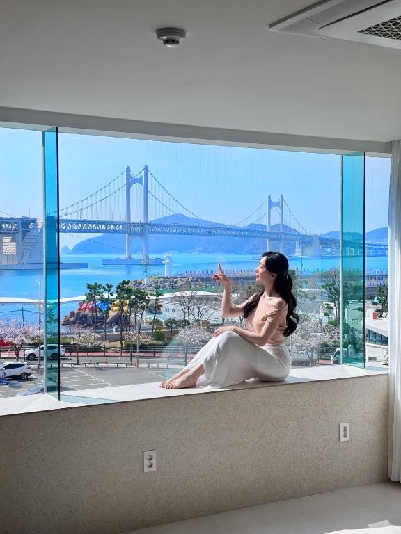 a woman sitting on a window sill looking out at a bridge at 광안사계스테이 GwanganSagyeStay in Busan
