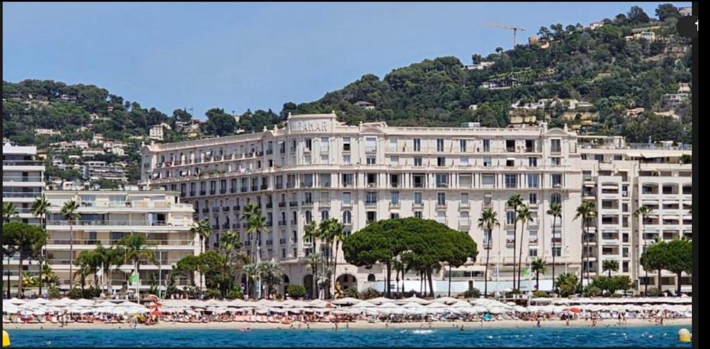 Hotel Palais Miramar, a large white building with umbrellas in front of a beach at Palais Miramar in Cannes