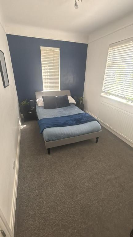 a bedroom with a bed with blue walls and two windows at Spacious Guest House Thornton Road, London in London