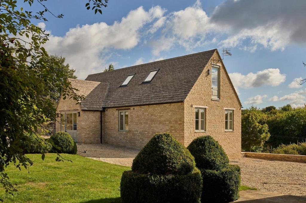 a brick house with two windows and some bushes at Stunning Cotswolds guest house in Chadlington