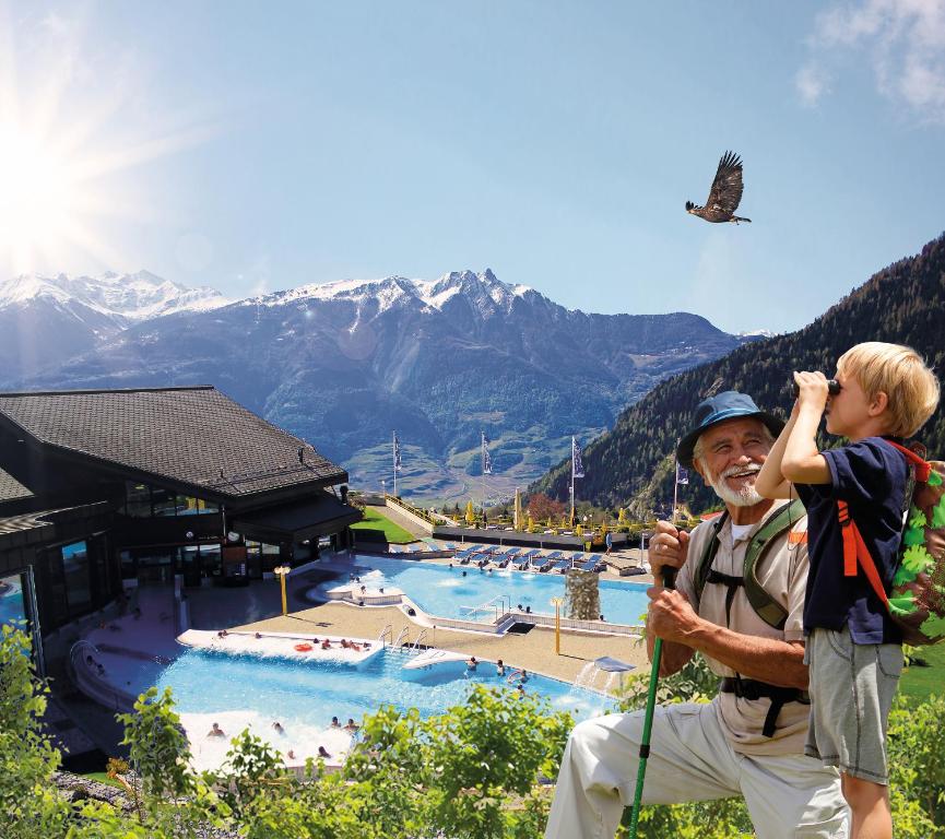 a man with a child on a back pack next to a pool at Hôtel des Bains d'Ovronnaz in Ovronnaz