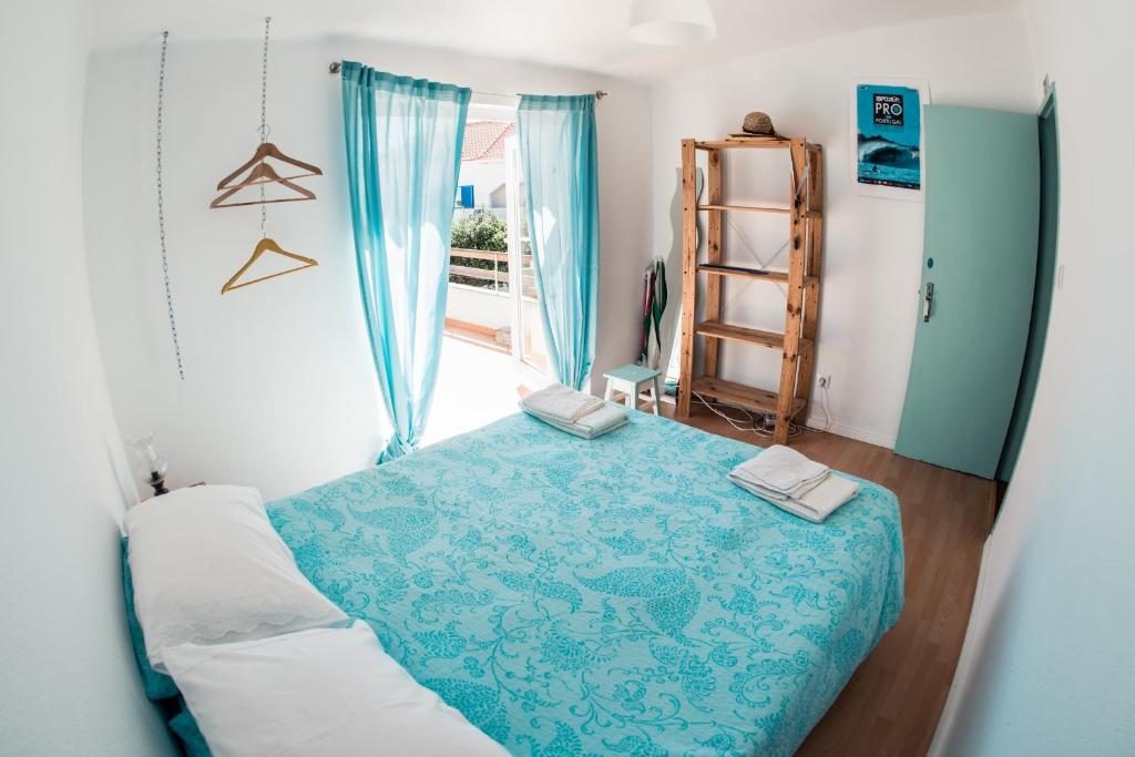 a bedroom with a bed with a blue blanket and a window at Native Surfhouse in Praia da Areia Branca