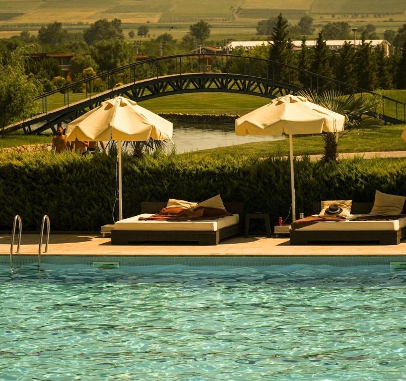 a pool with two umbrellas and two beds and a swimming pool at Villa Ambassadori Kachreti Golf Resort in Kachretʼi