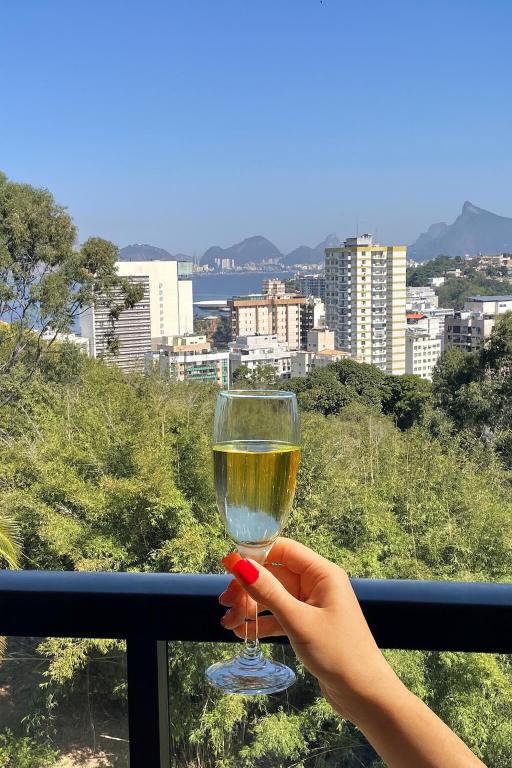 a person holding a glass of wine on a balcony at Varanda com Vista Mar - Cristo, Bondinho e Museu! in Niterói