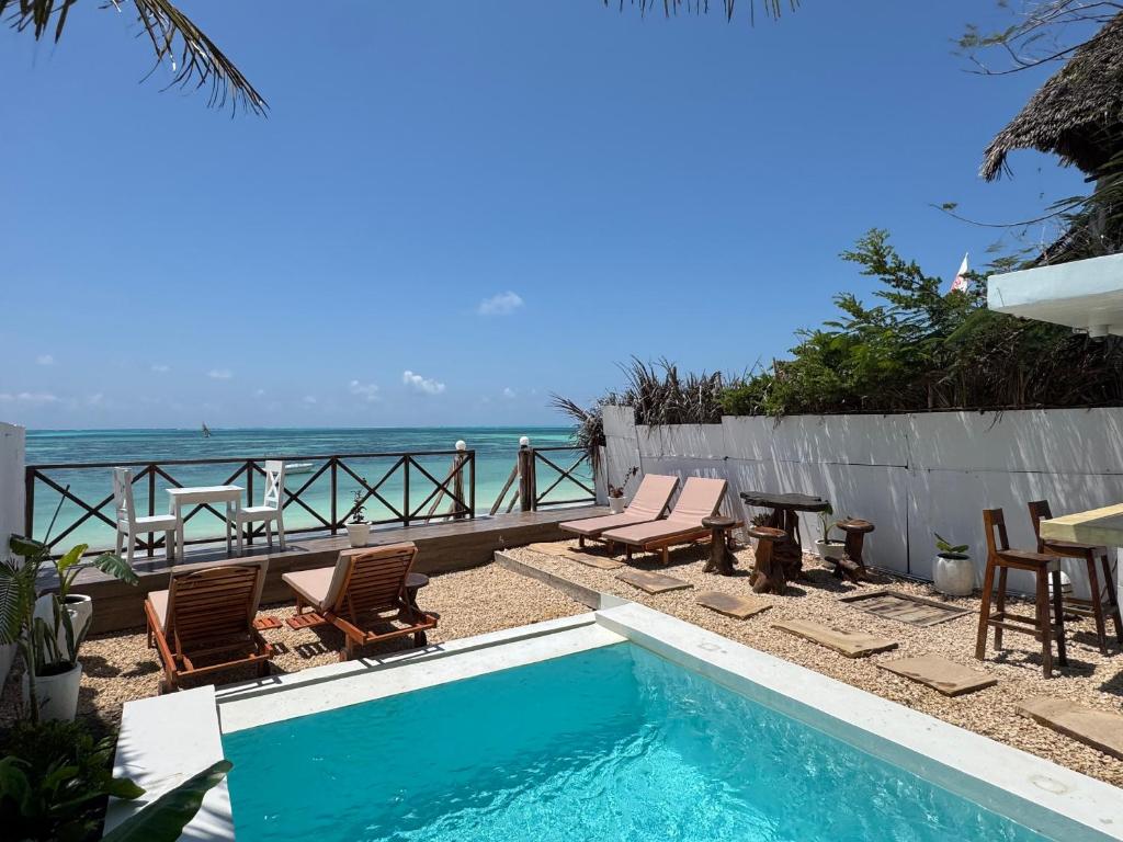 a swimming pool with chairs and a table and the ocean at ZAN Sun Beach in Makunduchi