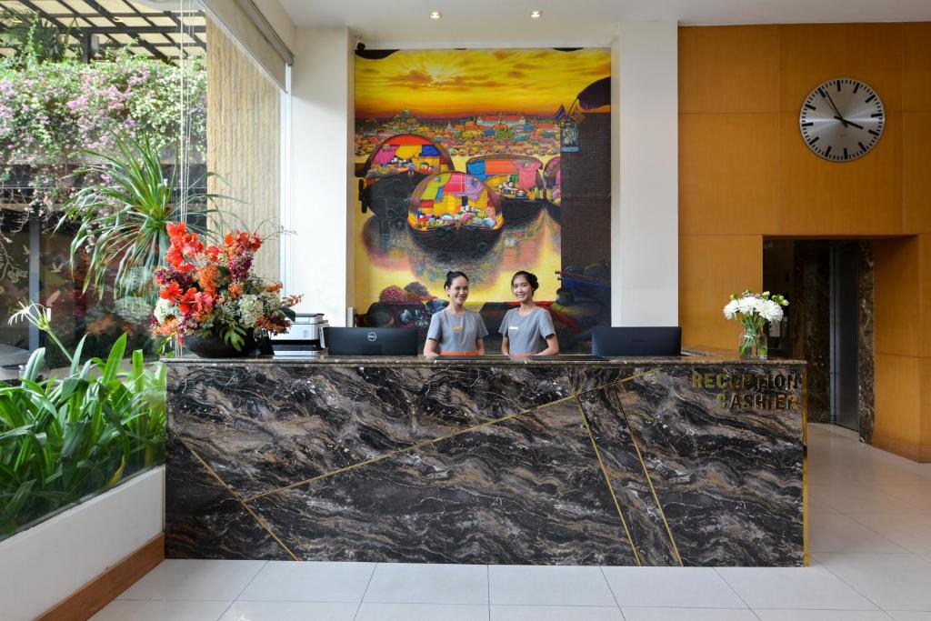 A staffed reception desk in a bright lobby filled with plants and artwork.