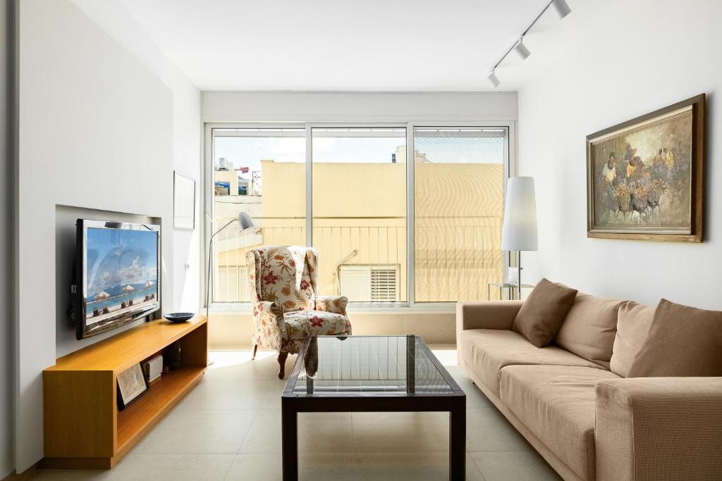 a living room with a couch and a tv at Chic Bright Urban Escape by Sea N Rent in Tel Aviv