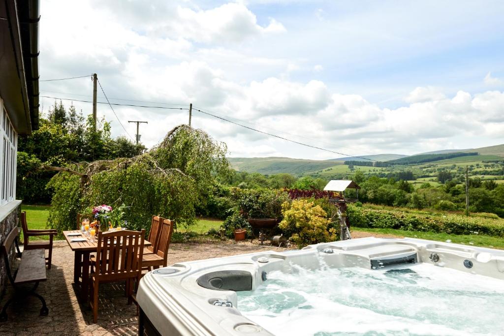 una bañera de hidromasaje en un patio con mesa y sillas en Bedlwyncoch Farmhouse, en Brecon