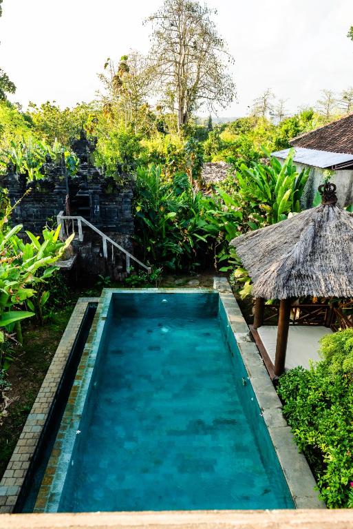 a swimming pool in a resort with a thatch roof at Balangan Bali Bungalow in Uluwatu