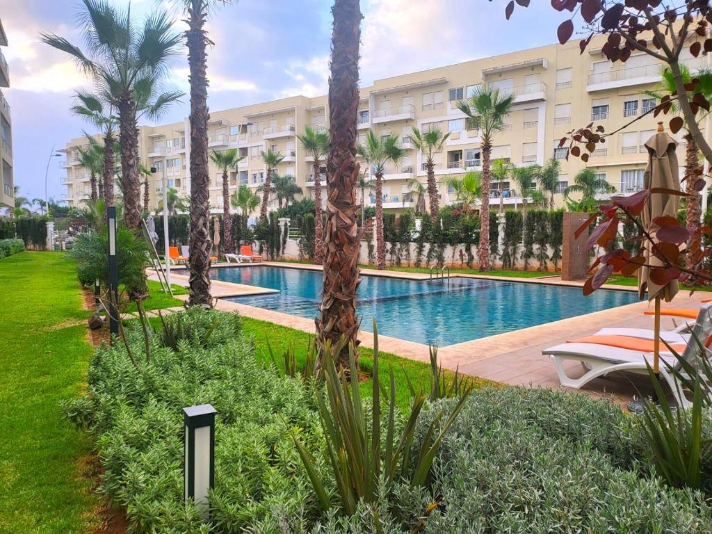 a resort pool with palm trees and a building at Superbe appartement à bouznika avec vue sur piscine et jardin privatif in Bouznika