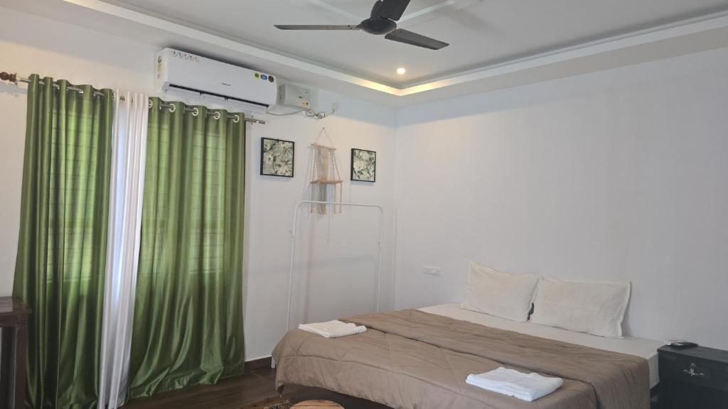 a bedroom with a bed with green curtains and a ceiling fan at Cascara Beach Resort in Varkala