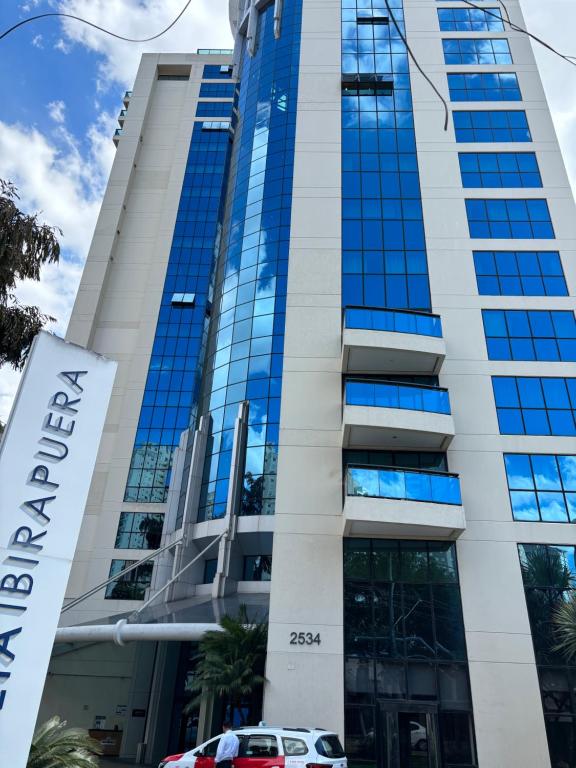 Un edificio alto con ventanas azules y un coche aparcado delante. en MLA Flat Hotel Moema Ibirapuera - Completo e ótima localização, en São Paulo