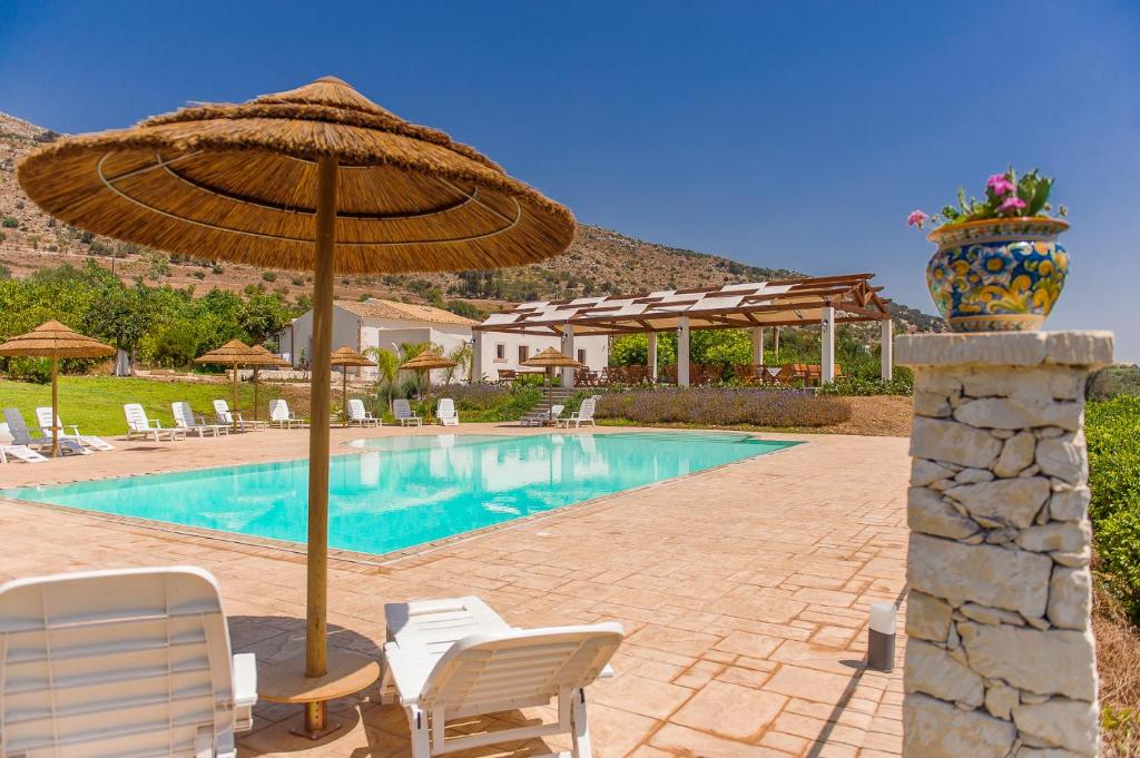 einen Pool mit einem Sonnenschirm, Stühlen und einem Tisch in der Unterkunft Agriturismo Alle Riserve Cavagrande in Avola