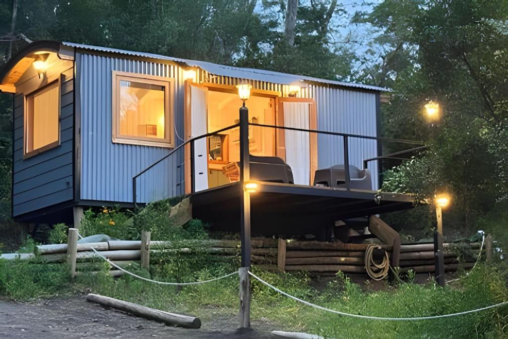 Una pequeña casa azul con porche y luces. en Escapada en pareja en un rincón del bosque, en San Martín de los Andes