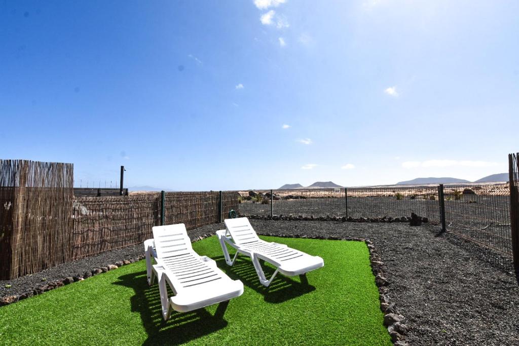 drei weiße Stühle sitzen auf dem Gras in der Nähe eines Zauns in der Unterkunft Book Jet - Bella Vista VIP Villa in Majanicho