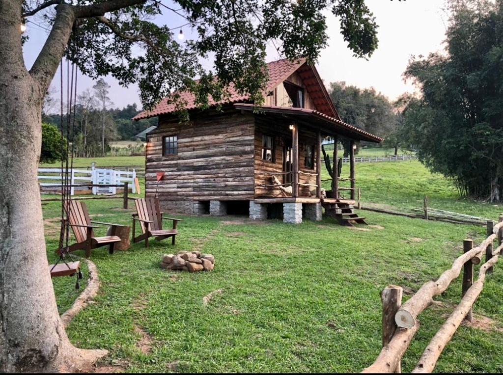une cabane en rondins dans un champ avec deux chaises et un arbre dans l'établissement Rancho SF Cabana Alabama, à Novo Hamburgo